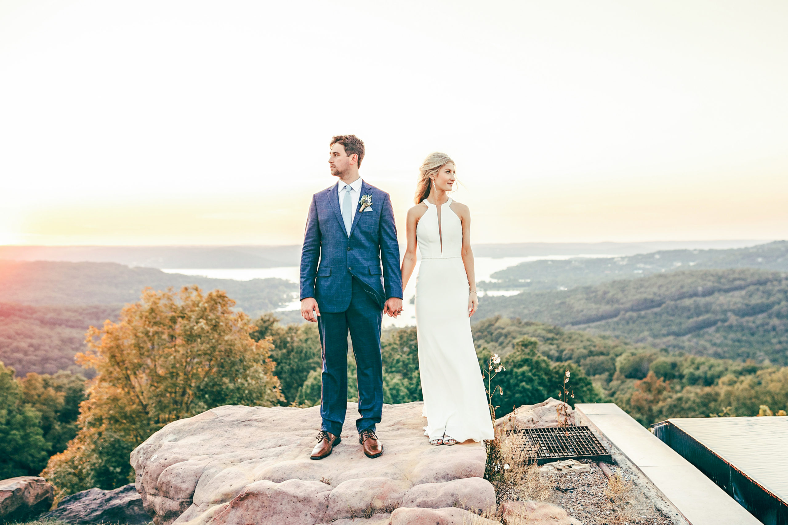 Bride and groom sunset and golden hour standing on a rock wide shot looking away from each other, Top of the Rock wedding venue in Branson Missouri Destination Weddings