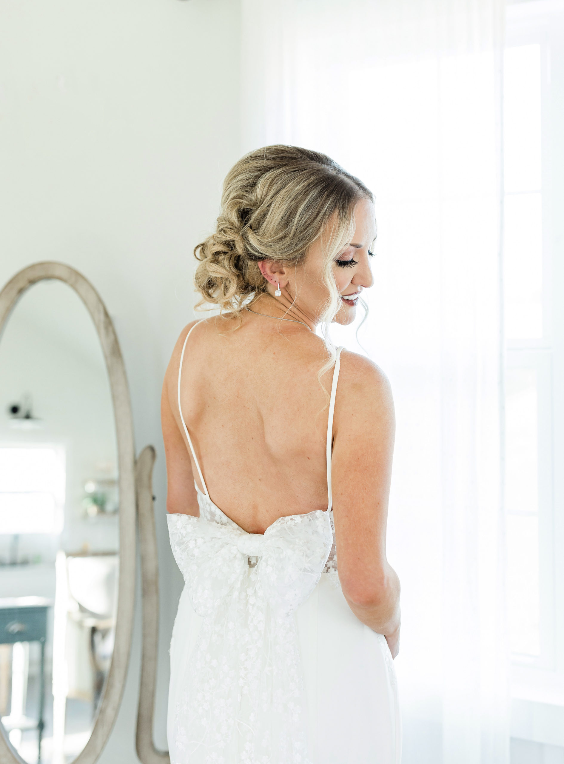 Bride smiles as she shows the back dress details of her dress captured by Tatyana Zadorin Photography. Close up of bride placing her hand on her chest showing off her ring and necklace taken in natural light