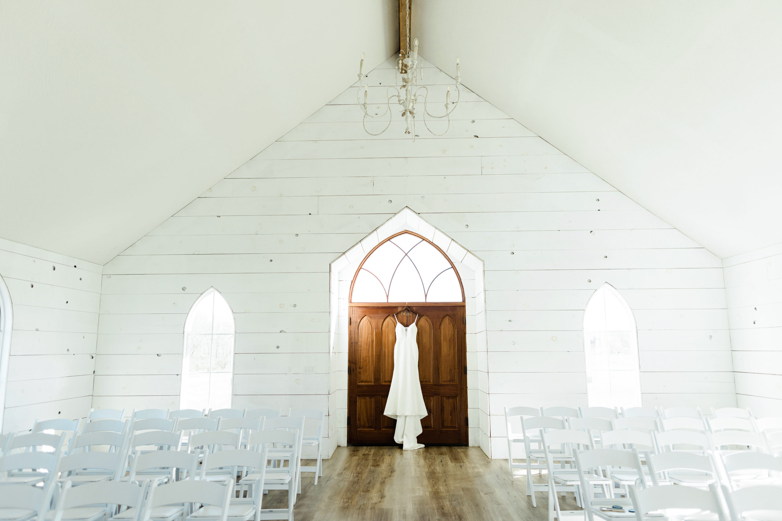 Wide angled shot of bride's wedding dress hung from a wooden door at the wedding venue, taken by Tatyana Zadorin Photography