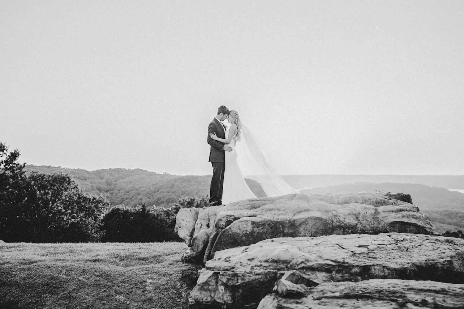 Black and white photo of bride and groom wrapping their arms around each other on a rock, taken by Tatyana Zadorin Photography