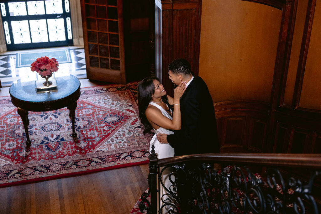 Intimate engagement portrait of a couple embracing at the top of the historic staircase inside the Aldredge House in Dallas, Texas.