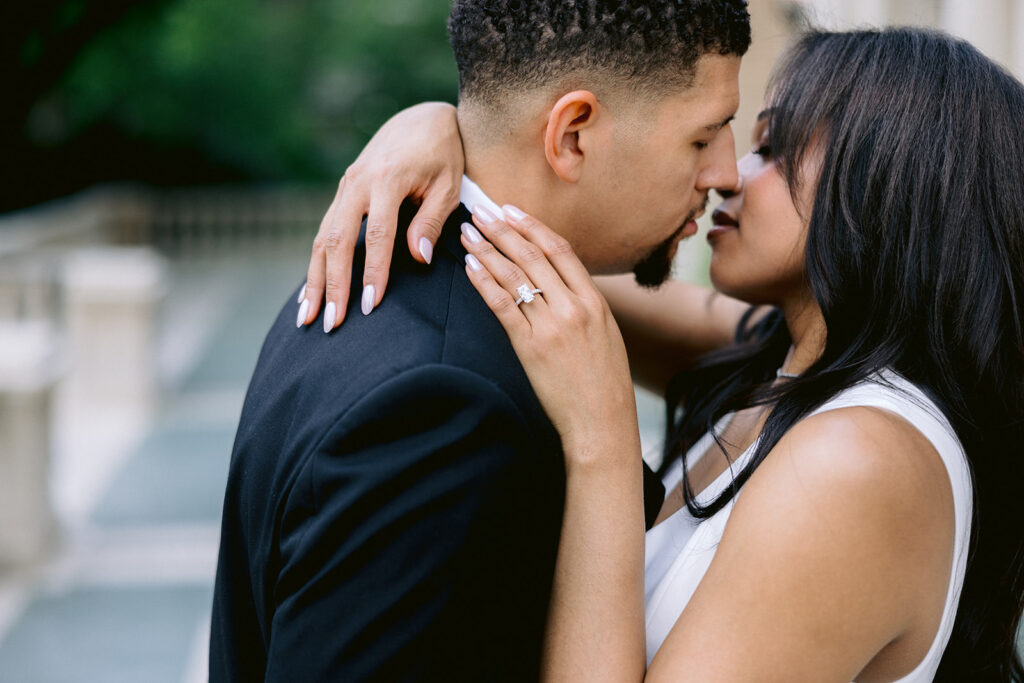 Close-up engagement photo featuring the bride-to-be's diamond engagement ring as she embraces her fiancé.