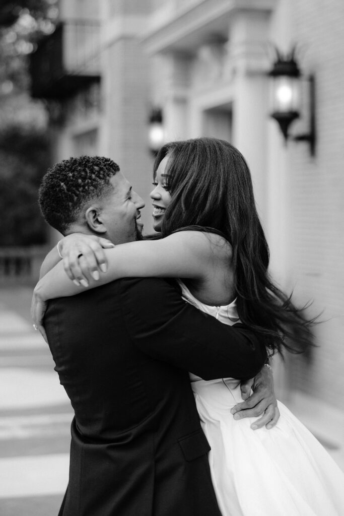 Black-and-white engagement photo of a couple embracing in front of the elegant Aldredge House mansion in Dallas.