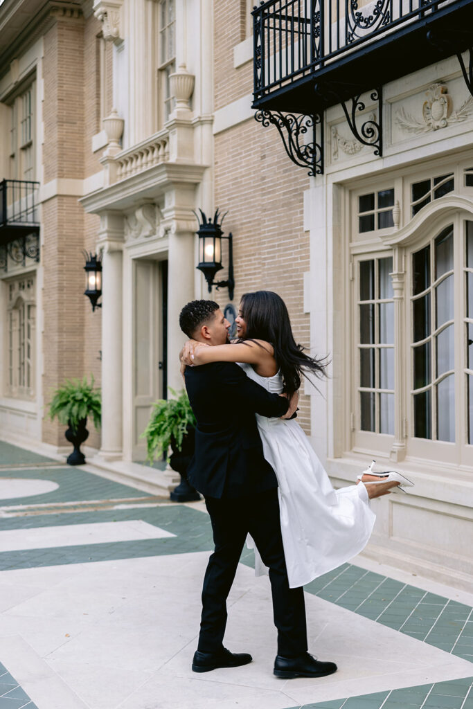 Romantic engagement photo of a groom lifting his fiancée during an elegant courtyard session at the Aldredge House.