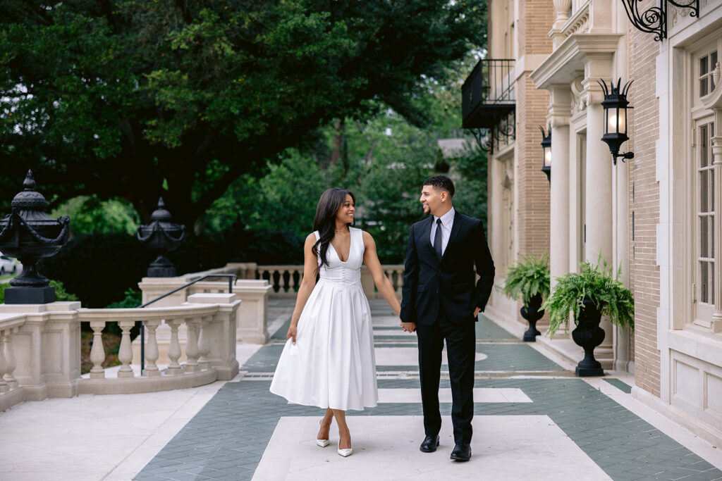 Elegant engagement photo of a couple walking together along the courtyard at the Aldredge House in Dallas.
