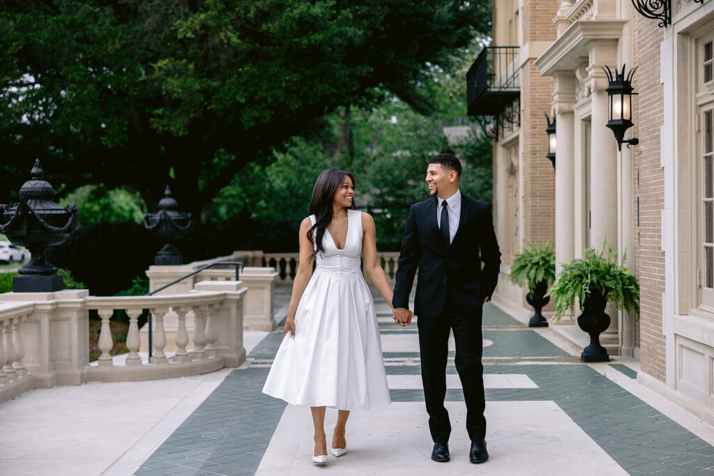 Romantic full-length engagement portrait of a couple strolling through the historic Aldredge House courtyard in Dallas, Texas.