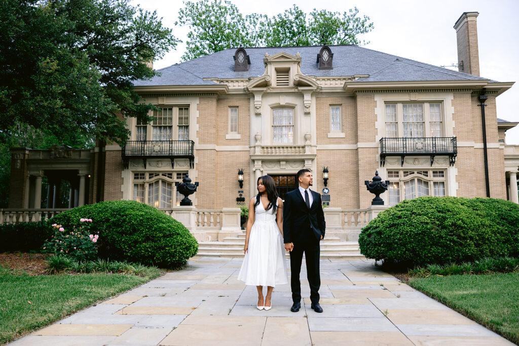 Elegant full-length portrait of an engaged couple standing in front of the historic Aldredge House in Dallas.