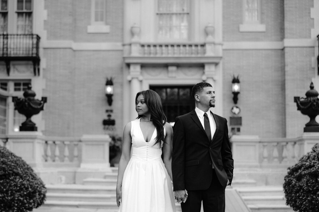 Timeless black-and-white engagement portrait of a couple walking together outside the Aldredge House in Dallas, Texas.