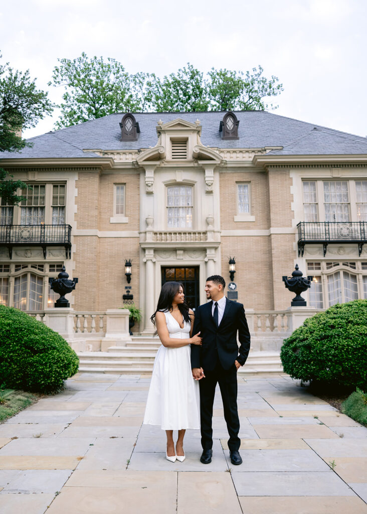 Elegant engagement portrait of a couple holding hands while walking in front of the Aldredge House in Dallas, Texas.