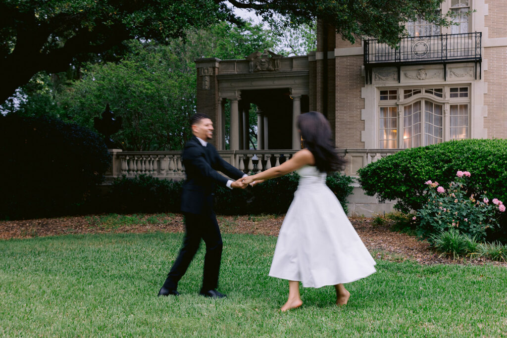 Playful engagement portrait of a couple twirling hand in hand during their Dallas engagement session at the Aldredge House.