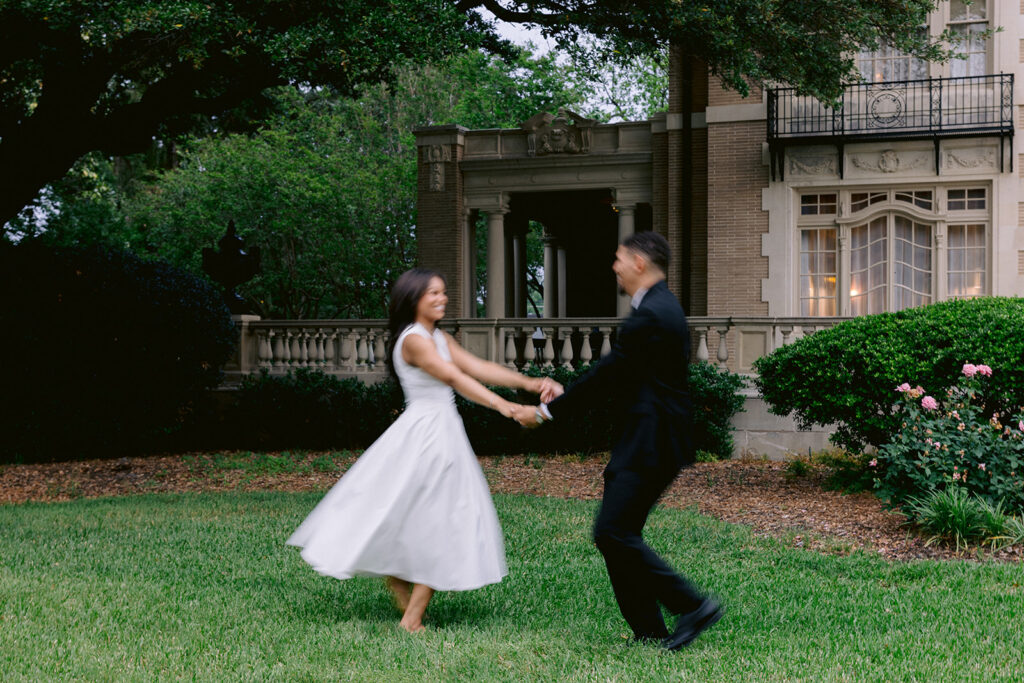Romantic engagement photo of a couple spinning together across the manicured gardens of the Aldredge House in Dallas.