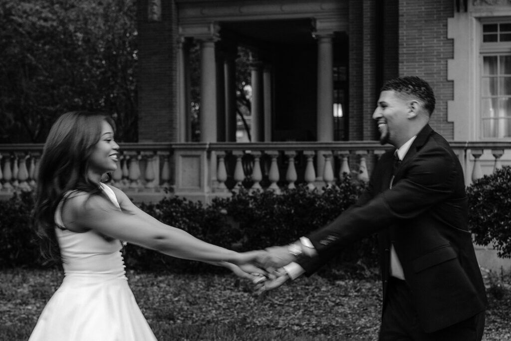 Joyful black-and-white engagement photo of a couple holding hands during an elegant outdoor engagement session in Dallas.