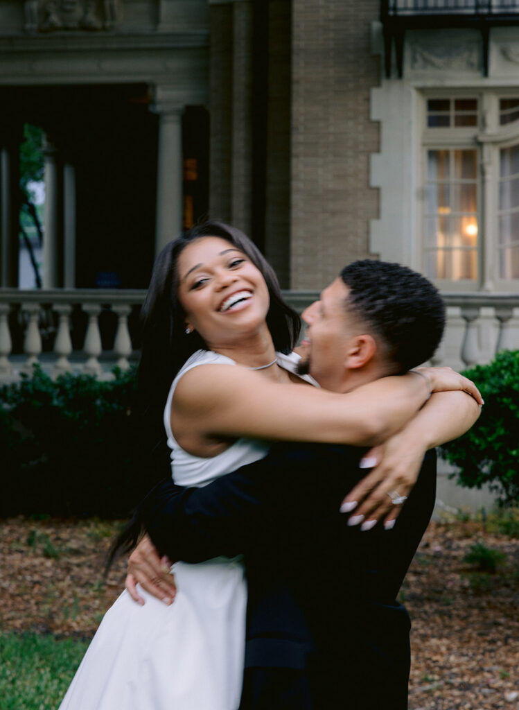 Bride-to-be embracing her fiancé with a joyful smile during a romantic engagement session at the Aldredge House.