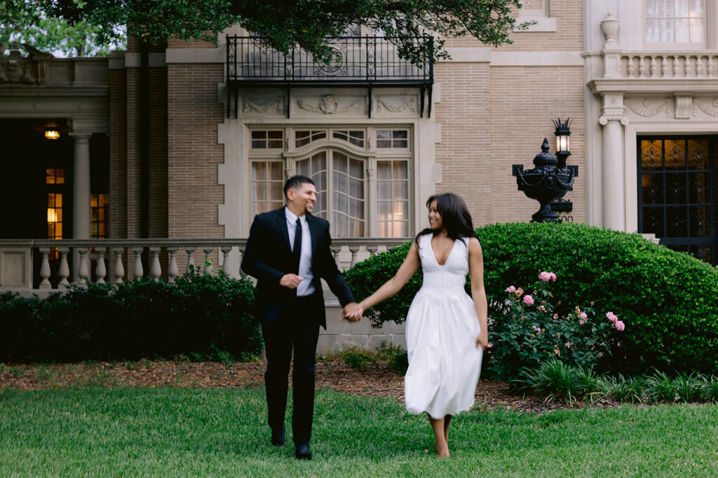 Natural engagement portrait of a couple walking hand in hand through the gardens of the historic Aldredge House in Dallas, Texas.