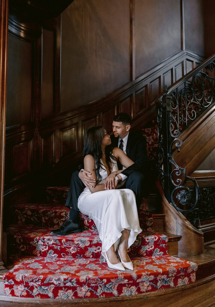Romantic engagement portrait of a couple sitting together on the grand staircase inside the historic Aldredge House in Dallas, Texas.