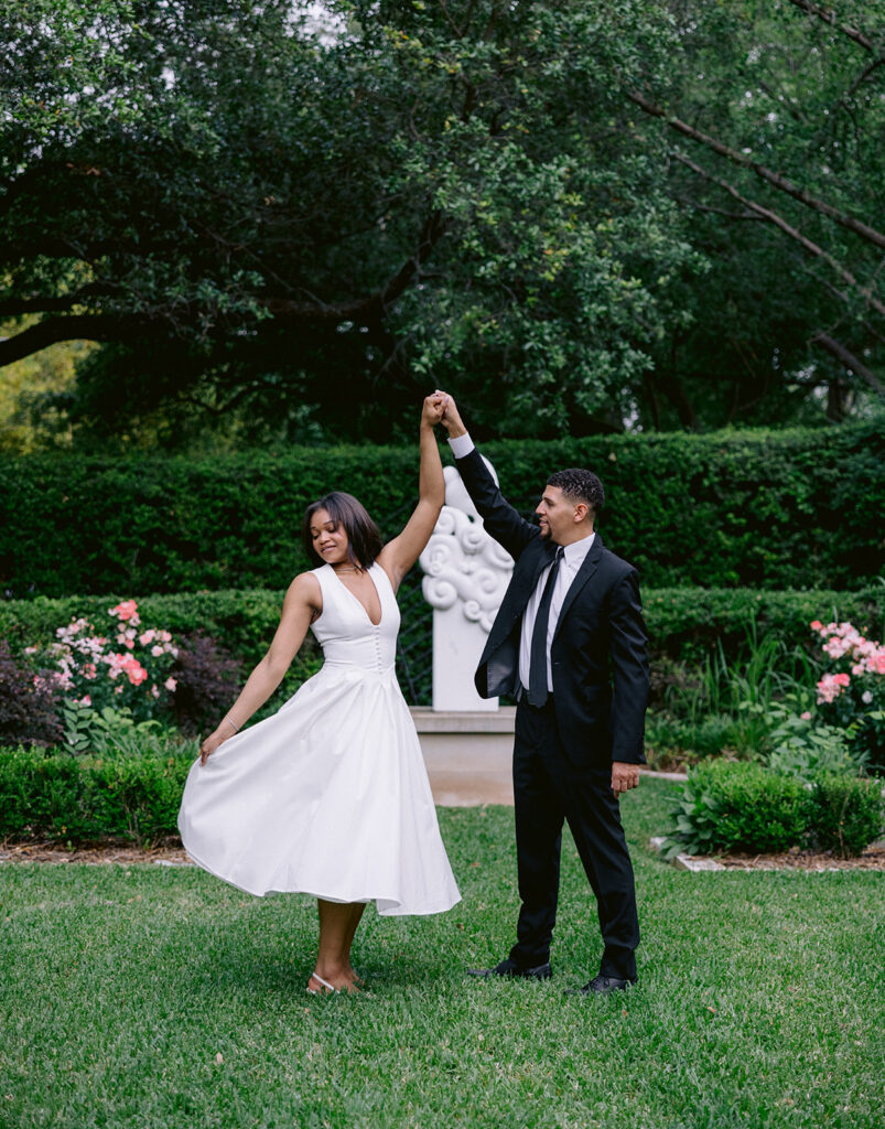 Bride-to-be laughing while standing with her fiancé beneath a classic white garden statue during their Dallas engagement session.