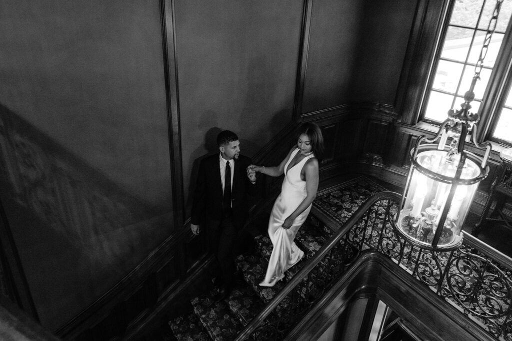 Editorial overhead engagement photo of a couple walking down the historic staircase inside the Aldredge House in Dallas.