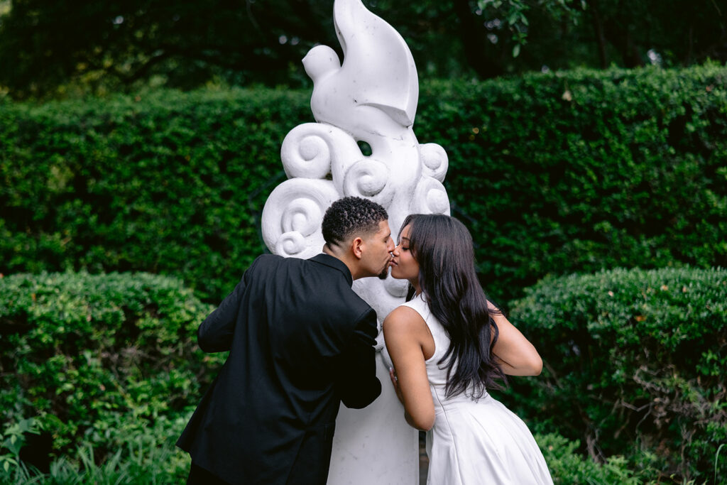 Close-up engagement portrait of a couple sharing an intimate moment beside a white sculpture in the gardens of the Aldredge House.