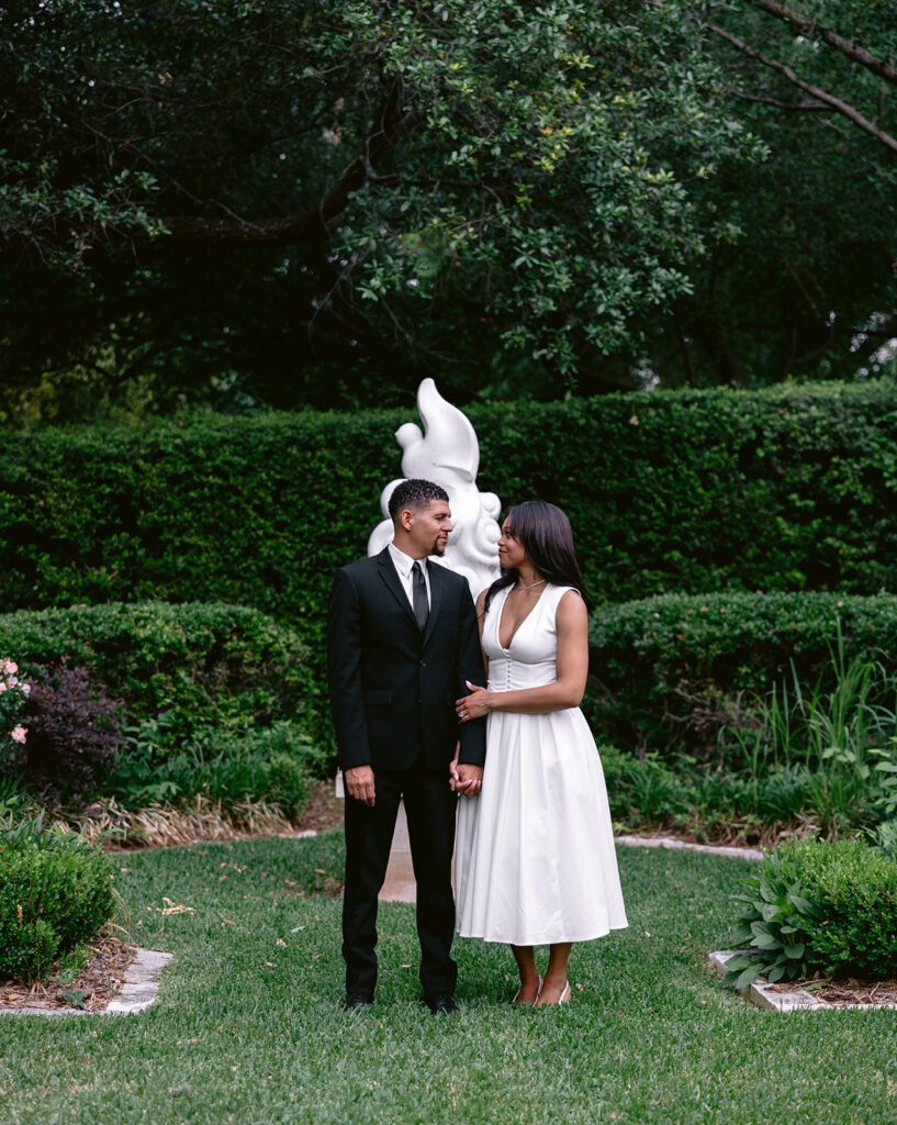 Romantic engagement portrait of a couple standing beneath a white garden sculpture at the Aldredge House in Dallas, Texas.