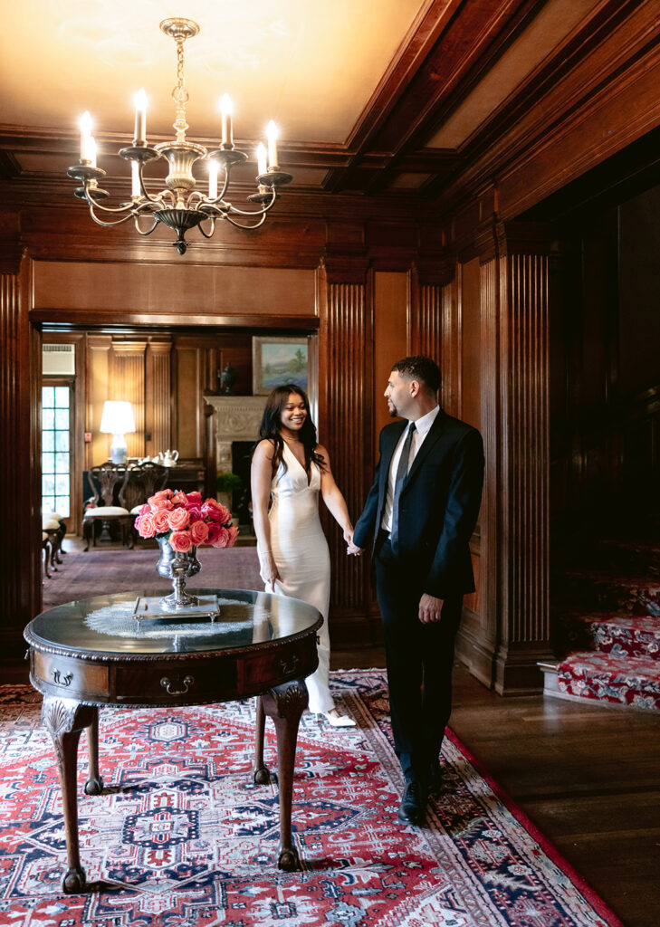 Timeless engagement portrait of a couple walking hand in hand through the elegant interior of the Aldredge House in Dallas, Texas.