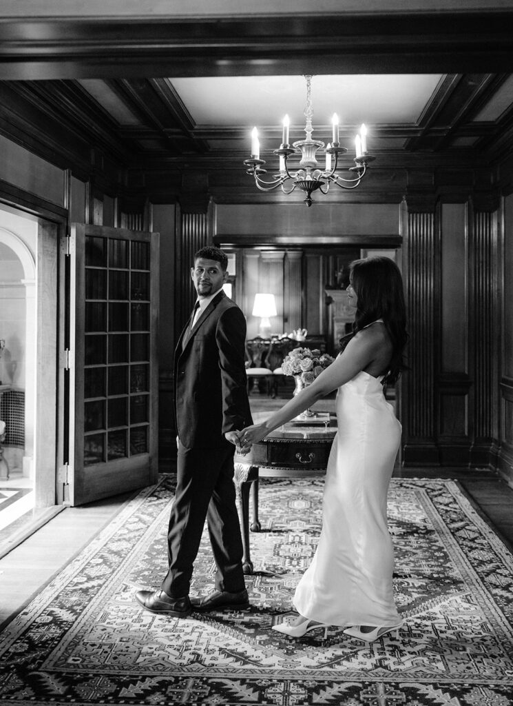 Editorial engagement portrait of a couple walking together through a grand historic room during their luxury Dallas engagement session.