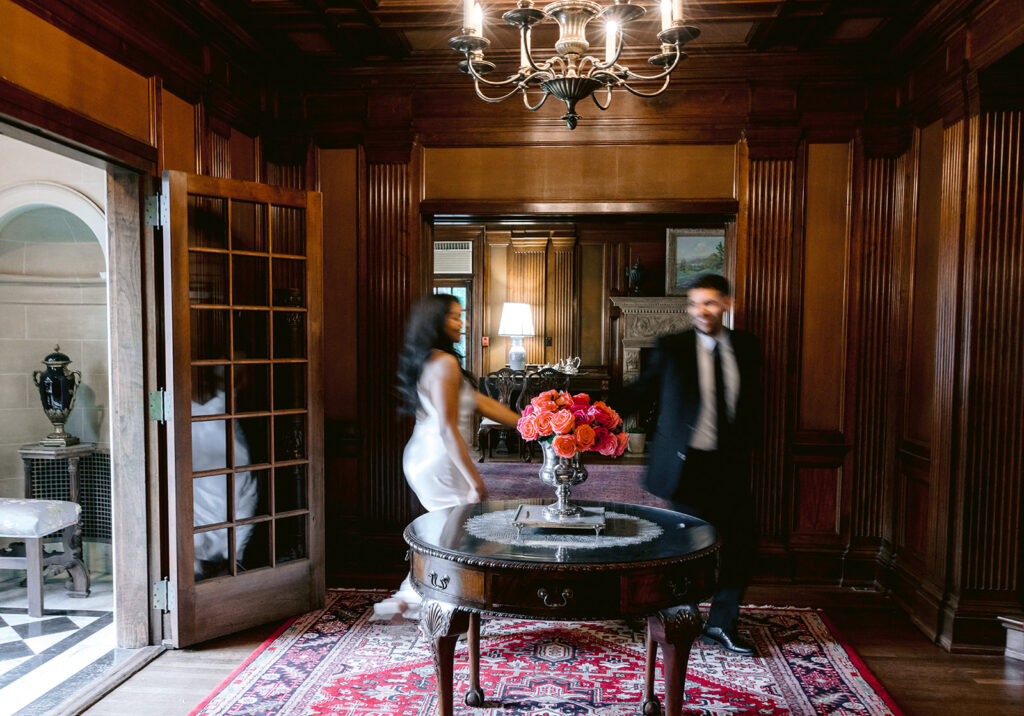 Editorial engagement photo of a couple walking together through the grand foyer of the historic Aldredge House mansion.