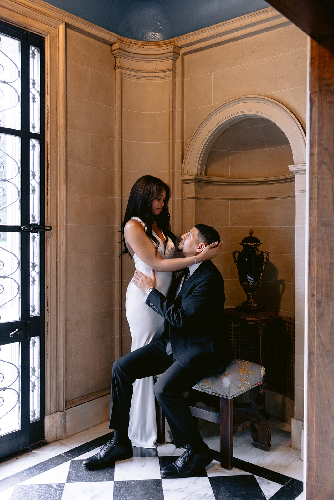 Romantic engagement portrait of a bride-to-be embracing her fiancé as he sits in the historic alcove of the Aldredge House.