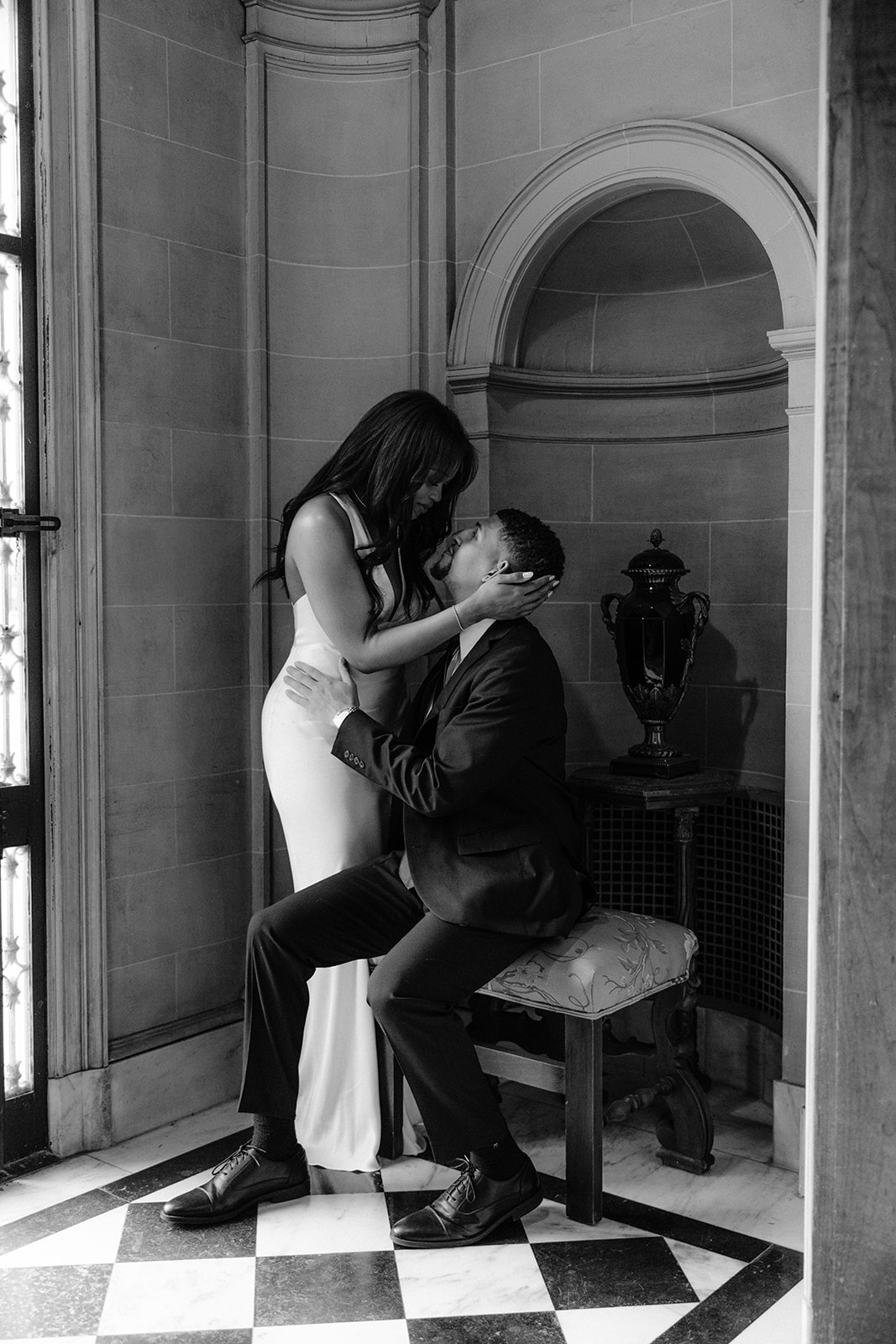 Elegant black-and-white engagement photo of a couple sharing an intimate moment in a historic stone alcove inside the Aldredge House.