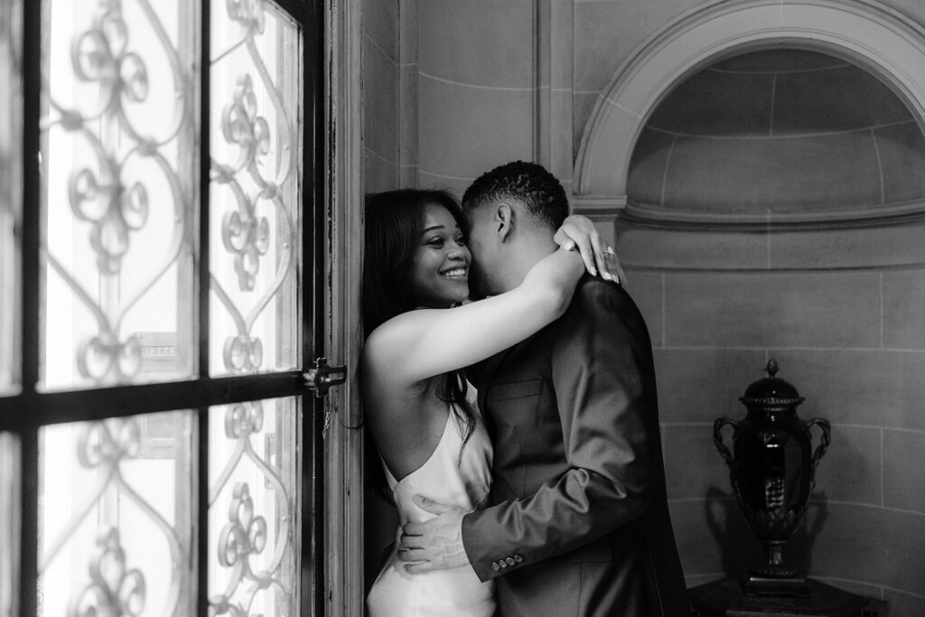 Elegant black-and-white engagement portrait of a couple embracing beside a grand window during their Dallas engagement session.