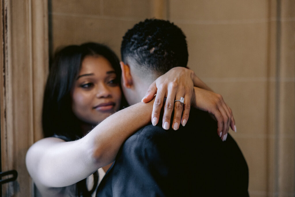 Close-up engagement photo featuring the bride-to-be's diamond engagement ring as she embraces her fiancé.