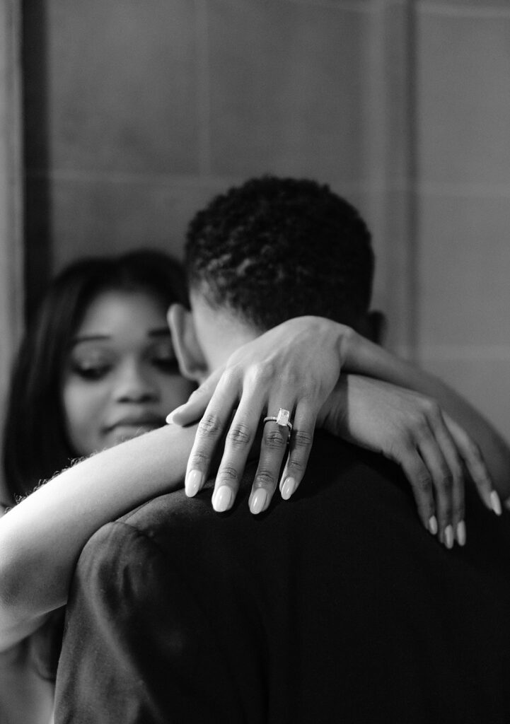 Timeless black-and-white close-up of a couple embracing, highlighting the bride-to-be's engagement ring during their Aldredge House engagement session.