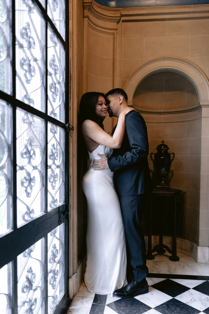 Elegant indoor engagement photo of a couple sharing a quiet embrace in the grand entryway of the Aldredge House mansion.