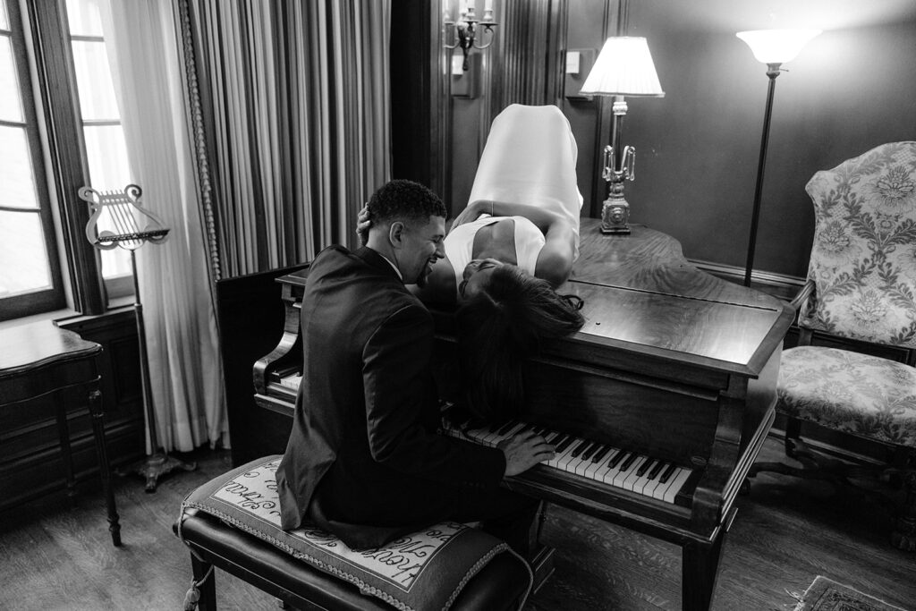 Black-and-white engagement photo of a couple embracing at a grand piano during their luxury Dallas engagement session.