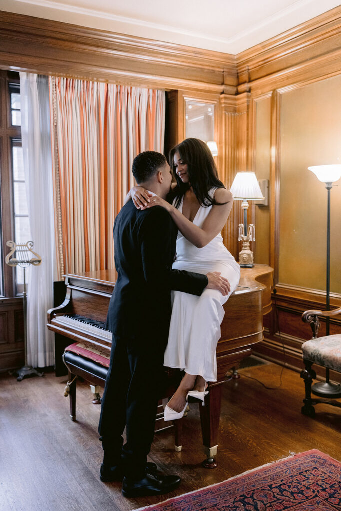 Elegant indoor engagement photo of a couple embracing in a historic music room filled with timeless architectural details.