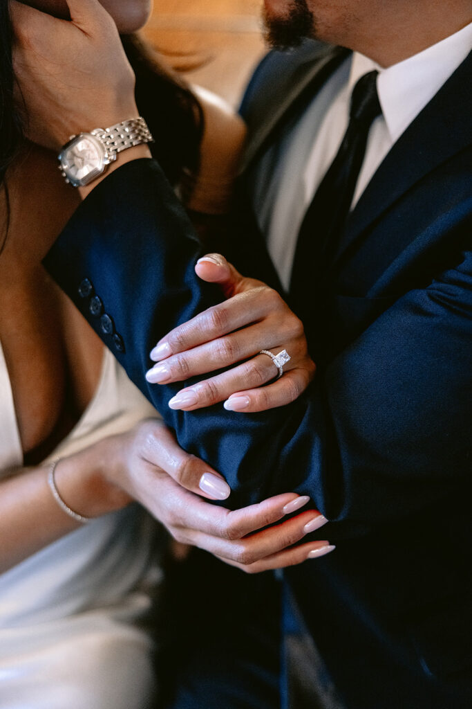 Close-up engagement portrait of the bride-to-be holding her fiancé's arm, showcasing her diamond engagement ring during their Dallas engagement session.