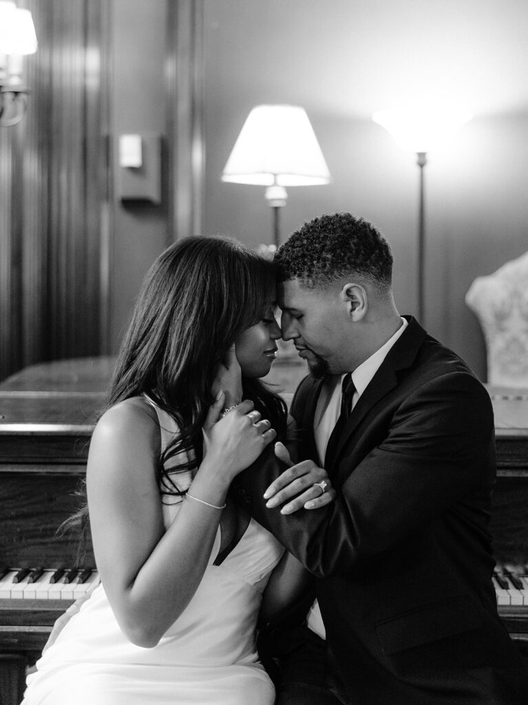 Timeless black-and-white engagement portrait of a couple sharing an intimate moment beside a grand piano inside the historic Aldredge House in Dallas, Texas.