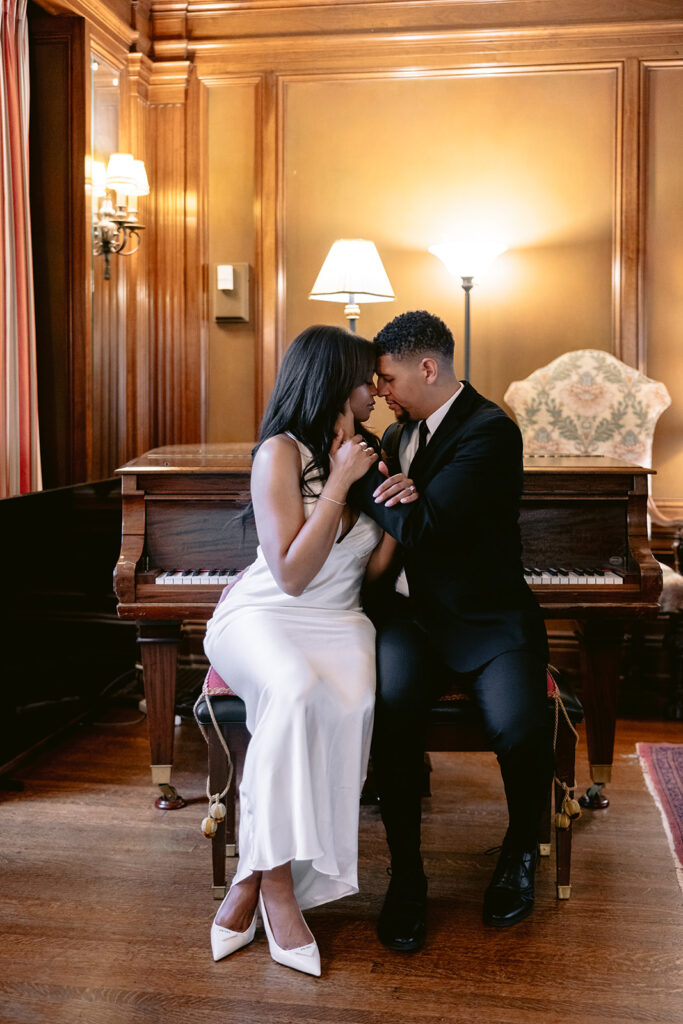 Elegant engagement photo of a couple sitting together at a grand piano during their luxury indoor engagement session at the Aldredge House.