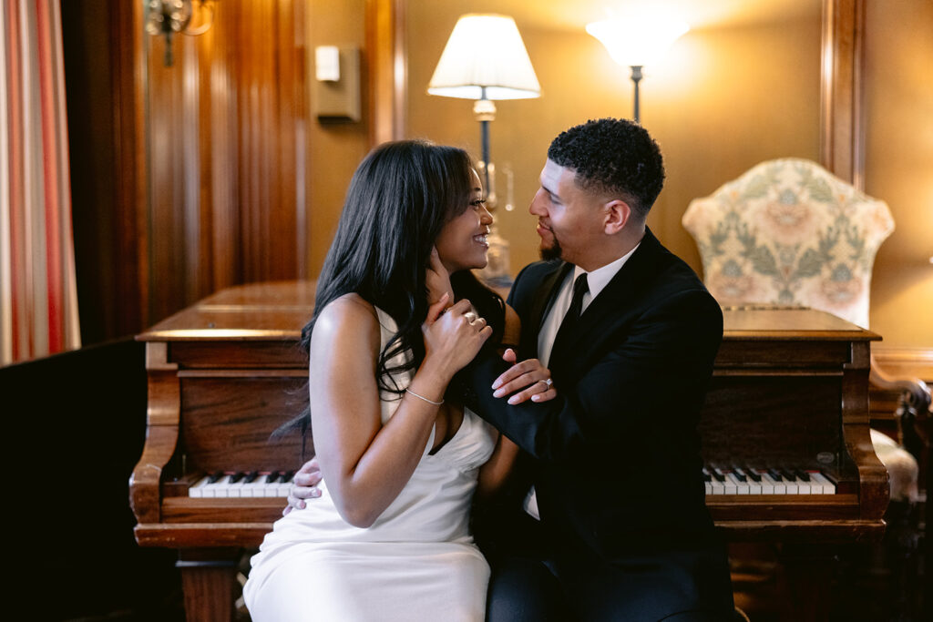 Joyful engagement photo of a couple smiling at each other in the elegant piano room of the Aldredge House in Dallas.