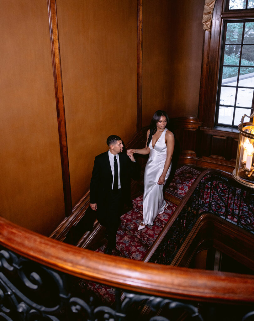 Elegant overhead engagement portrait of a couple pausing together on the ornate staircase inside the historic Aldredge House.