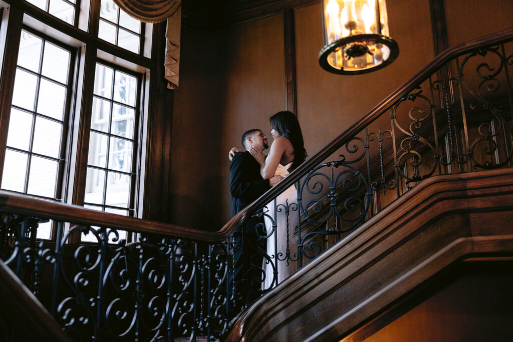 Romantic engagement portrait of a couple embracing on the grand staircase inside the historic Aldredge House in Dallas, Texas.