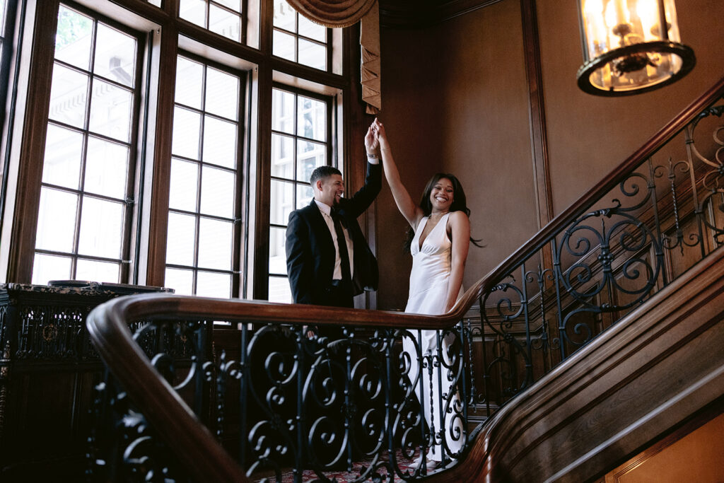 Elegant engagement photo of a couple holding hands on the grand staircase inside the historic Aldredge House mansion.