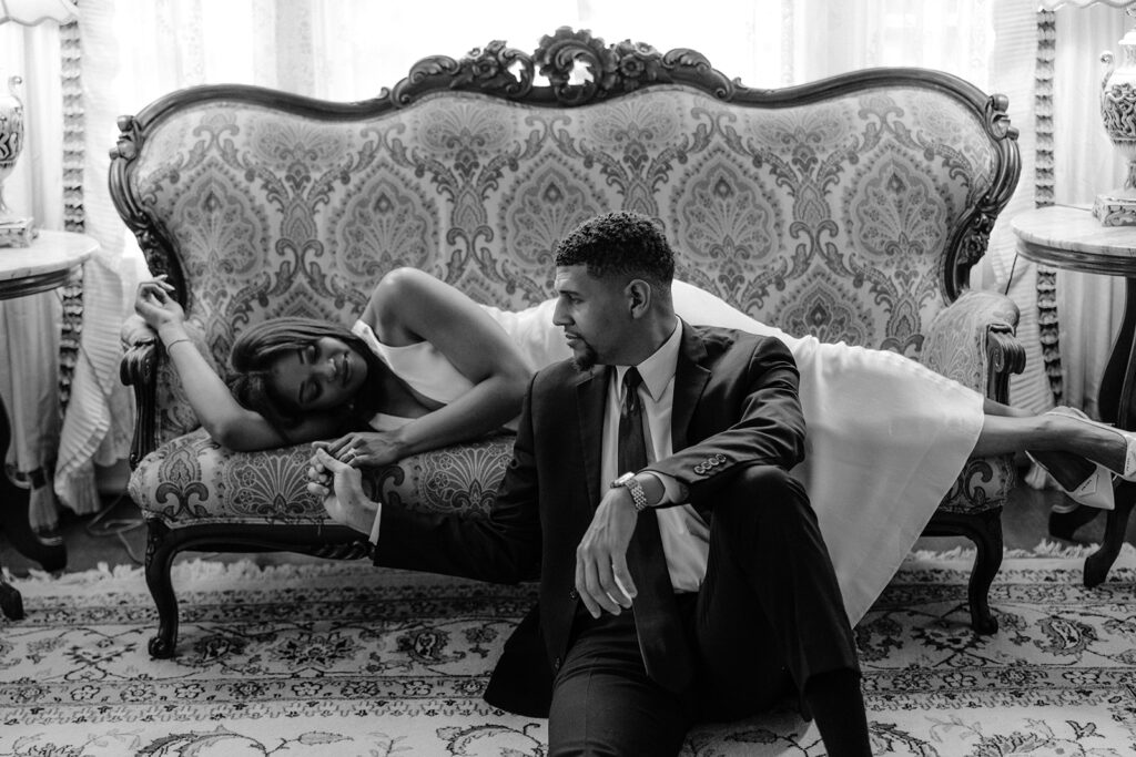 Timeless black-and-white engagement portrait of a couple relaxing on an antique sofa inside the historic Aldredge House in Dallas, Texas.