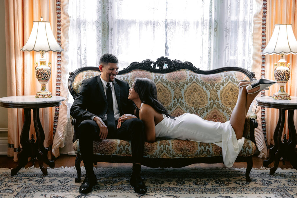 Luxury engagement portrait of a couple sitting together on a vintage sofa inside the historic Aldredge House in Dallas.