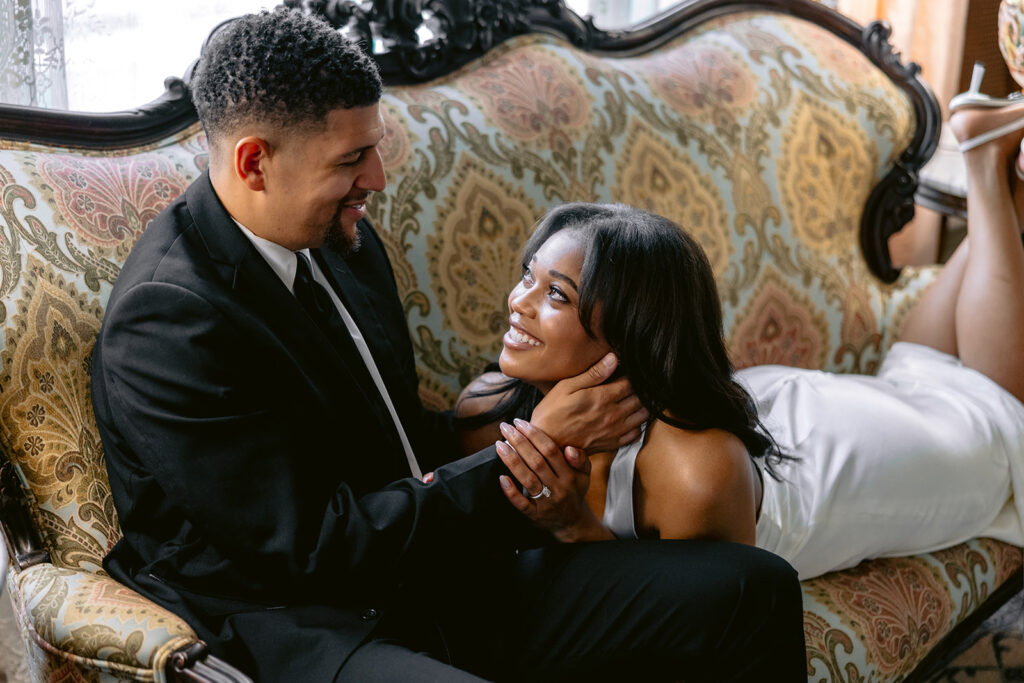 Intimate engagement photo of a couple sharing a joyful moment on a vintage sofa during their Dallas engagement session.