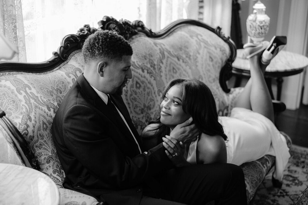 Timeless black-and-white engagement portrait of a couple cuddling together inside the historic Aldredge House mansion.