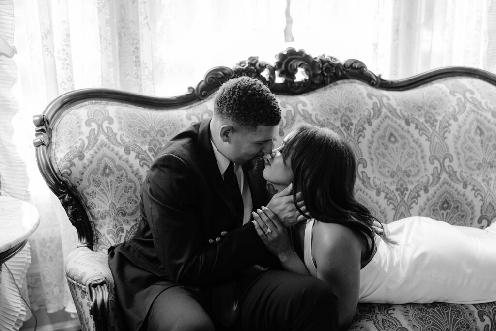 Timeless black-and-white engagement photo of a couple embracing on a vintage sofa during their Aldredge House engagement session.
