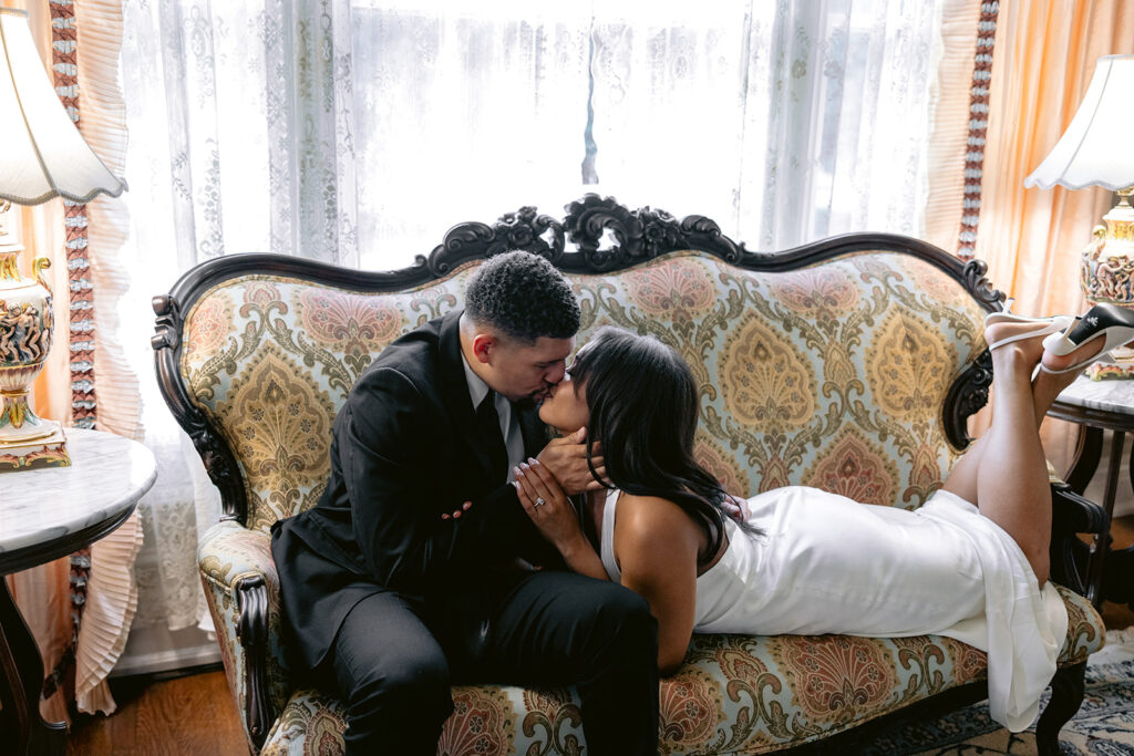 Luxury indoor engagement portrait of a couple cuddling on an elegant antique sofa inside the Aldredge House mansion.