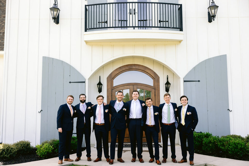 Classic groom and groomsmen portraits featuring the wedding party in black suits with blush floral boutonnieres, captured outside The French Farmhouse wedding venue in Collinsville, Texas before the wedding ceremony.