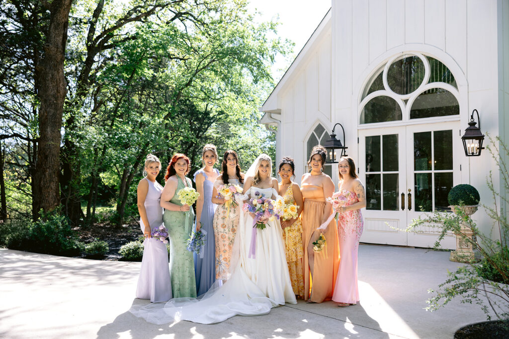 Elegant bridesmaid portraits featuring the bride with her bridal party in colorful pastel dresses, lush spring bouquets, and joyful outdoor wedding photos at The French Farmhouse wedding venue in Collinsville, Texas.