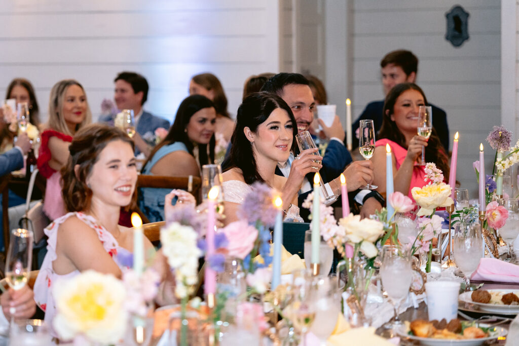 Elegant wedding reception toasts featuring heartfelt speeches, joyful laughter from the bride and groom, emotional guest reactions, and beautifully decorated sweetheart table at The French Farmhouse wedding venue in Collinsville, Texas.